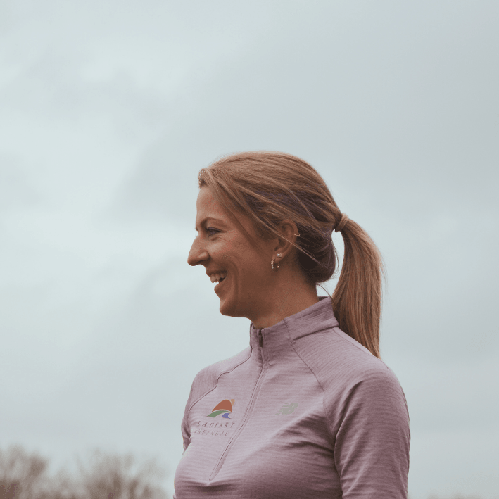 Läuferin mit lila New Balance Laufjacke im Freien vor bewölktem Himmel