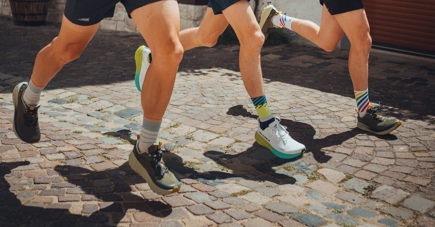 Drei Läufer im Test mit Laufschuhen auf Kopfsteinpflaster, bunte Sportsocken, Vergleich