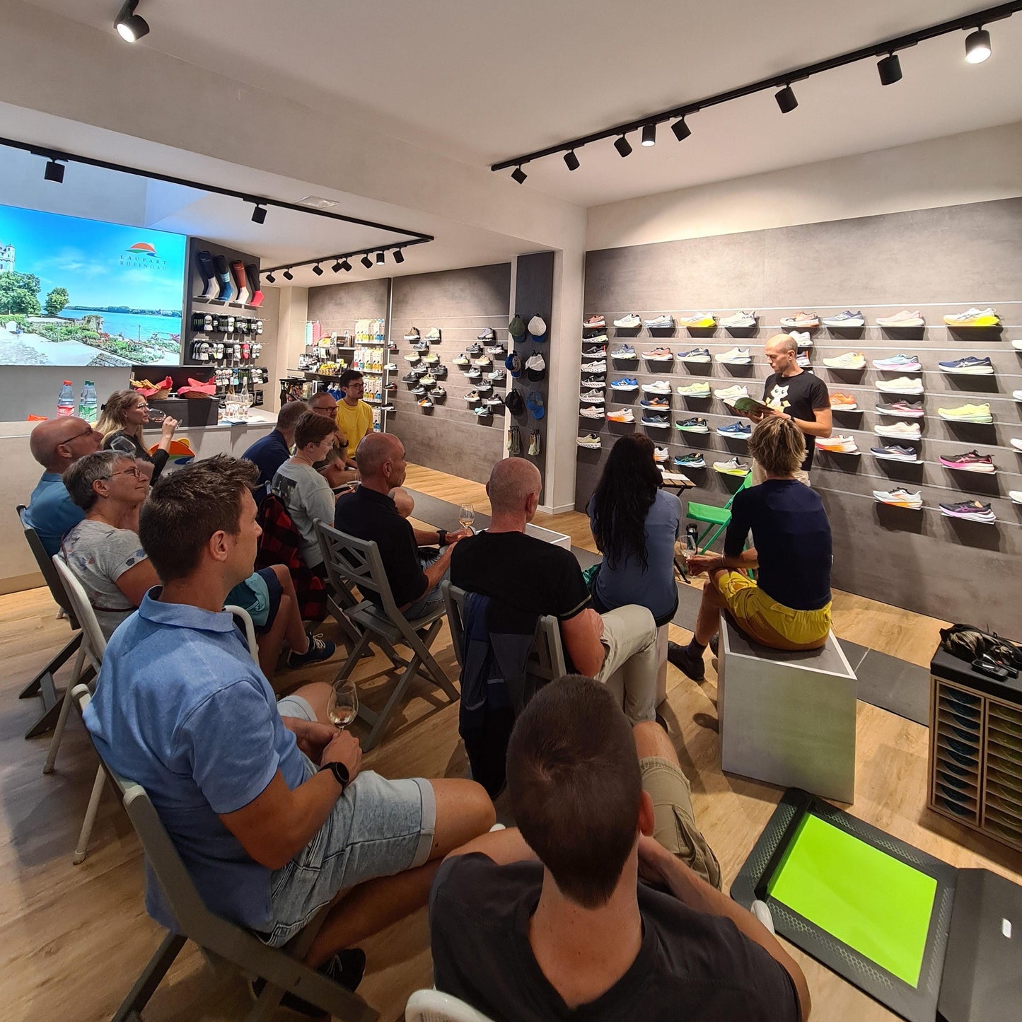 Lesung in modernem Laufschuhgeschäft mit Publikum, Regalen voller Sportschuhe und Vortragendem