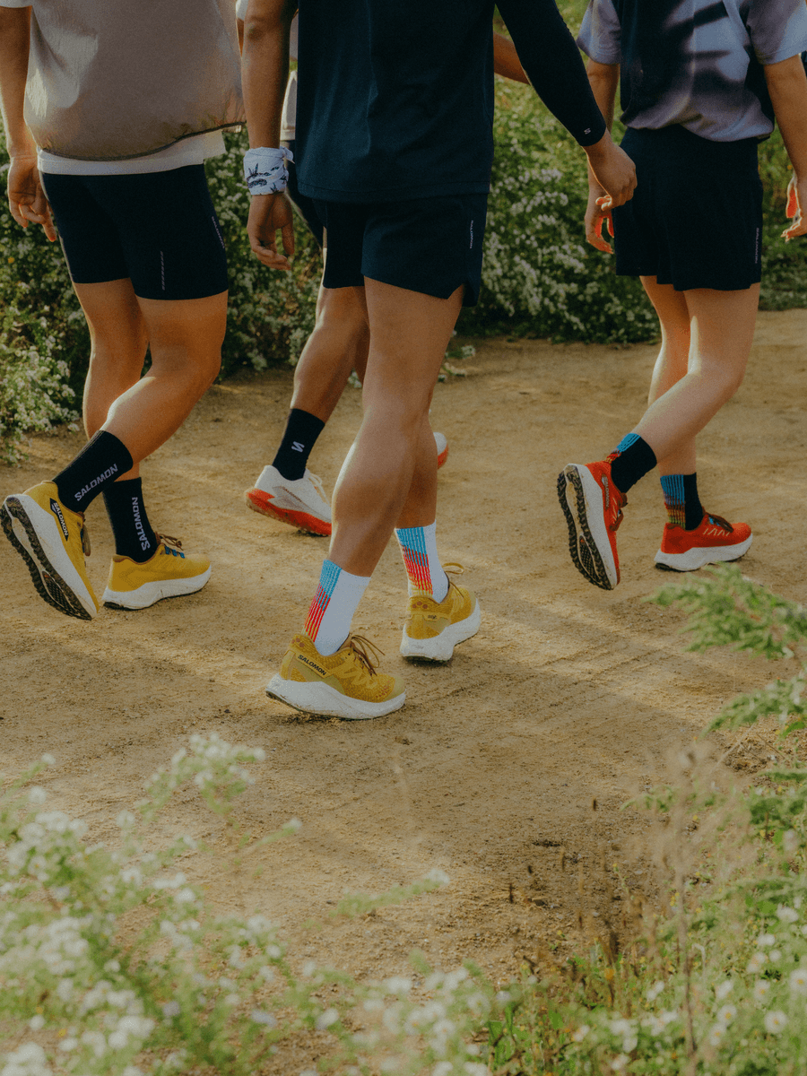 Gruppe läuft mit bunten Laufschuhen und Salomon-Socken auf Naturweg im Grünen