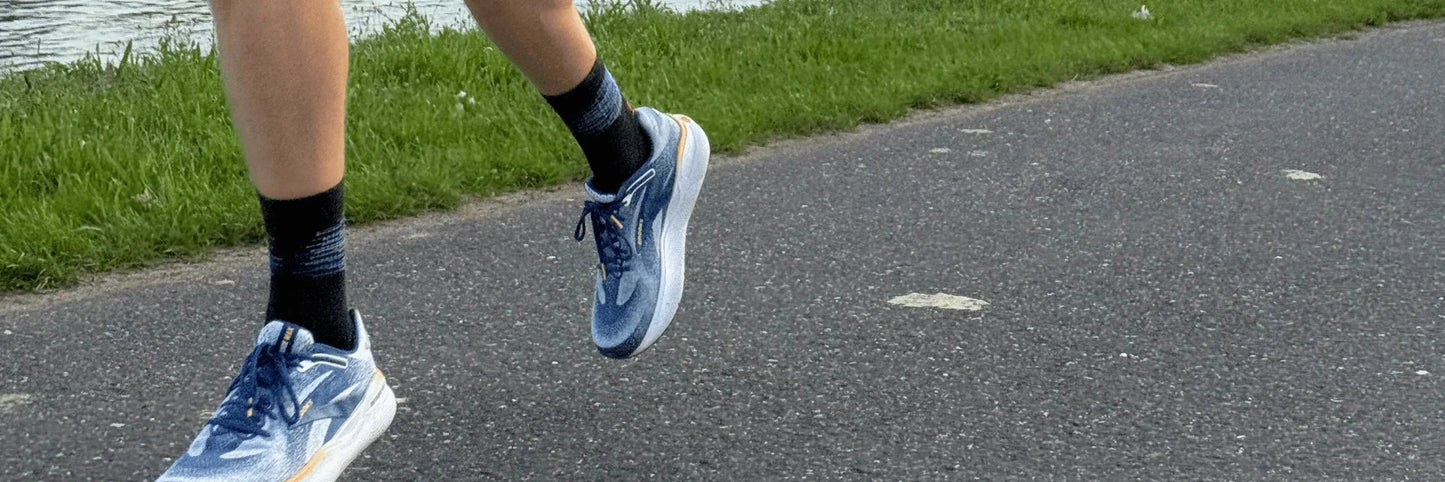 Läufer mit blauen Brooks Defyance Max Neutralschuhen joggt auf Asphaltweg am Wasser