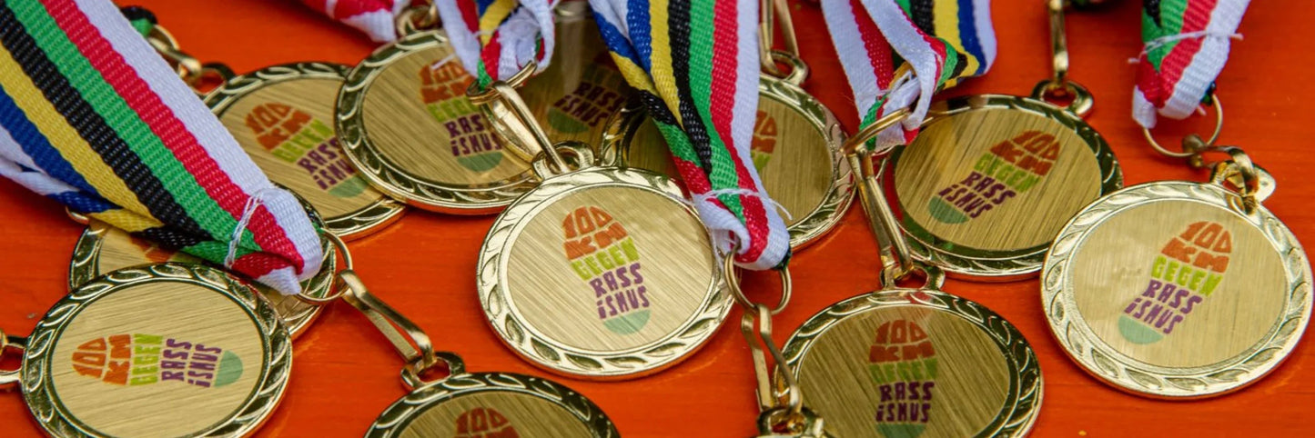 Goldene Medaillen mit bunter Bändchen, Aufschrift '100km gegen Rassismus'
